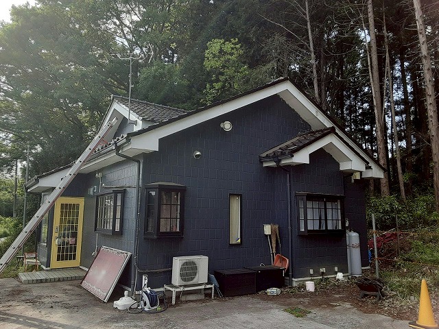 現場調査を行うため屋根にはしごをかけている店舗建物の外観