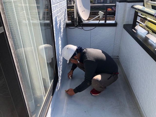ベランダ防水メンテナンス下地処理工程でメッシュテープを貼り付ける職人