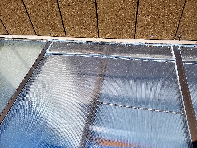 サンルームの屋根に別の屋根材を仮設置してコーキング処理を施している状況