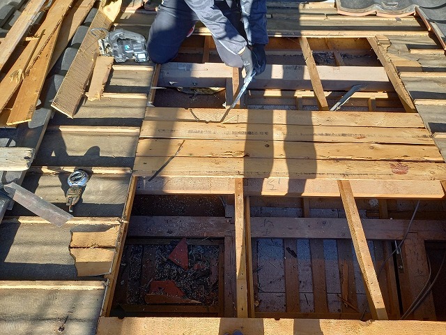 屋根葺き直し工事で損傷を受けたバラ板をバールで取り除いている状況