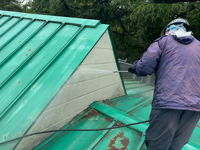 屋根の妻壁部分に高圧洗浄機で水を吹き付けて洗浄している様子