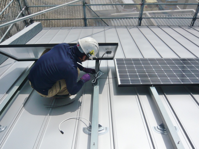 ２階建て住宅の屋根に太陽光パネルの設置工事を行っています。