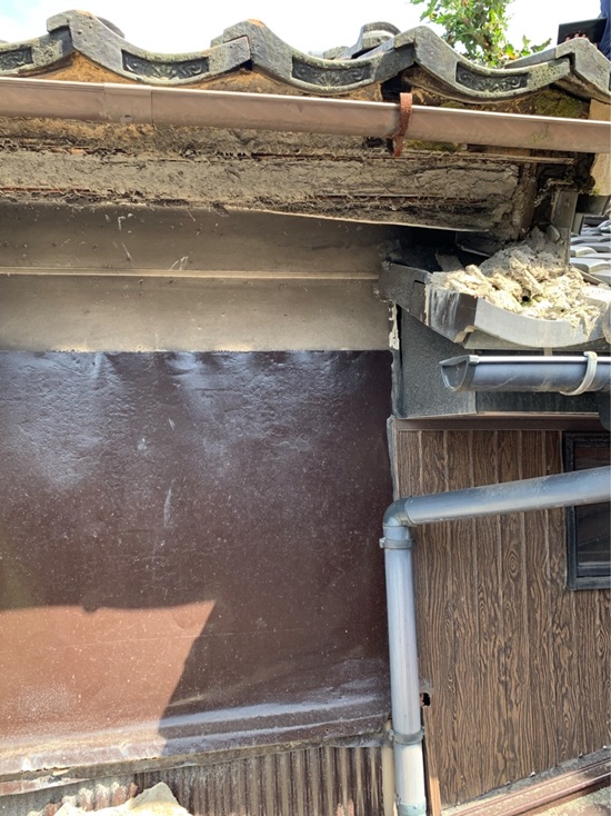 屋根の先端にあたる鼻隠し（屋根の先端で、雨樋が設置されている部分）、軒天（屋根が外壁より突き出している部分の天井にあたるところ）部分の白壁が崩れて、白壁や土が屋根の上に散らかっています。