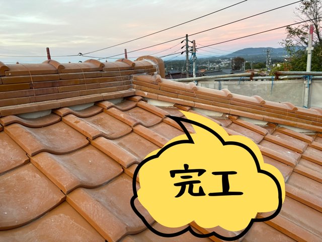 屋根の棟積み替え工事が完了した状態。のし瓦と冠瓦がきれいに並び、周囲の景色が見える夕方の仕上がり写真