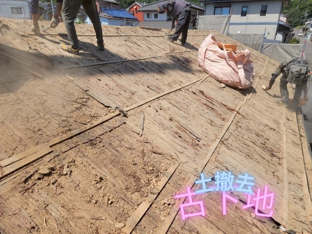 職人が屋根の葺き土を剥がして古い木製下地を露出させている作業風景