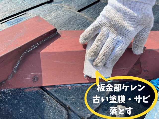軍手で研磨紙を持ち、赤茶色の棟板金表面をケレンしている作業手元。