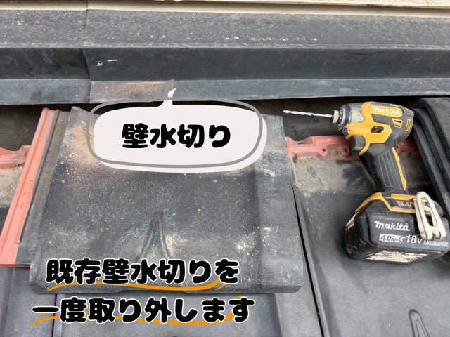 瓦屋根の壁際にある黒い水切り板金と、インパクトドライバーが置かれている様子。古い壁水切りを取り外す前の状態
