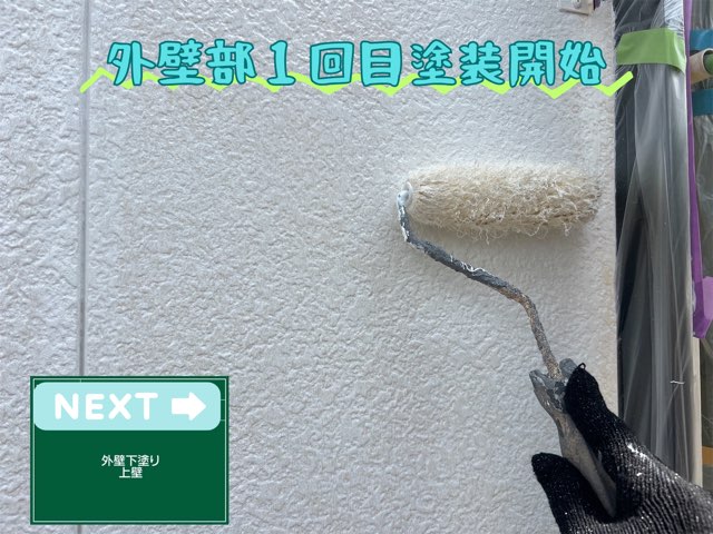 上部の外壁に白い下塗り材をローラーで塗布している様子。