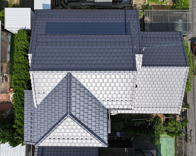 施工後の屋根全景。栄四郎瓦プラウドUU40Gが美しく均一に並び、棟や谷板金も新しく整えられた仕上がり。色ムラがなく陰影がきれいに出た、耐久性の高い葺き替え完了後の屋根をドローンで撮影した写真。