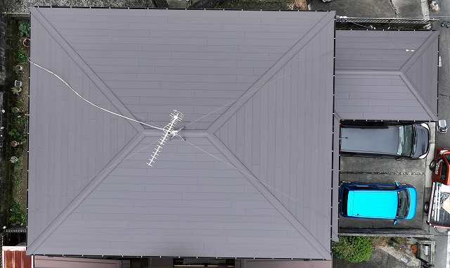 多治見市松坂町にて屋根カバー工事と雨樋交換工事が完了した住宅の屋根全景。ドローンで上空から撮影した寄棟屋根で、屋根材が均一に施工され、雨樋も建物外周にきれいに取り付けられている様子が確認できる。