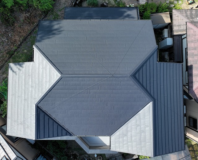 多治見市幸町にて実施したカバールーフ・外壁塗装工事の完工後の様子。屋根全体が均一な濃いグレーに仕上がり、光沢のある美しい仕上がりが確認できるドローンからの俯瞰写真。