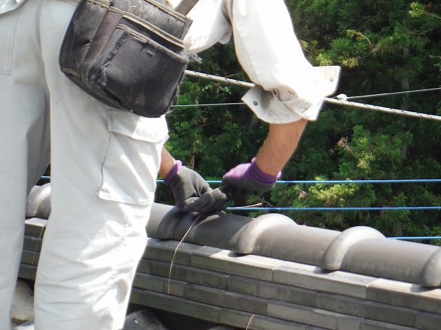 銅線を使って重なった瓦を固定している作業員
