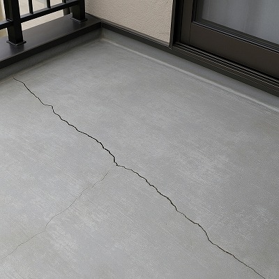 ベランダ床の表面に細かいクラックが入っている様子。FRP防水が硬化し、温度差で発生したひび割れの拡大を示す写真