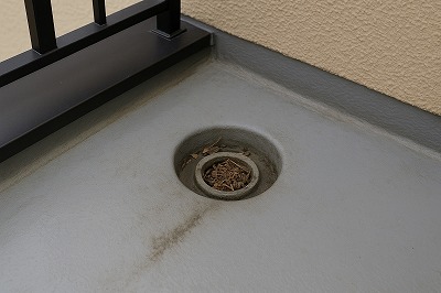 ベランダの排水口に土埃やゴミが溜まり、水が流れにくくなっているドレン詰まりの状態を写した写真