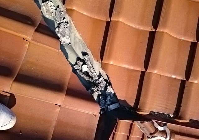 谷板金にこびりついた古い漆喰とゴミの拡大写真。銅板自体に穴はないが、堆積物が雨水の流れを堰き止めている危険な状態。