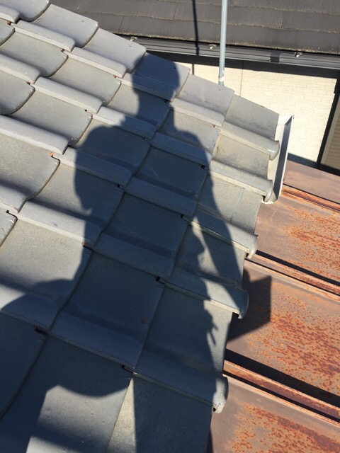 瓦屋根とサビた金属屋根の境界部分を細かく点検し、最適な施工方法を検討する様子