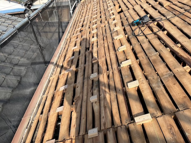 下地の不陸調整。パッキンを差し込み、屋根の波打ちをミリ単位で平滑にする。