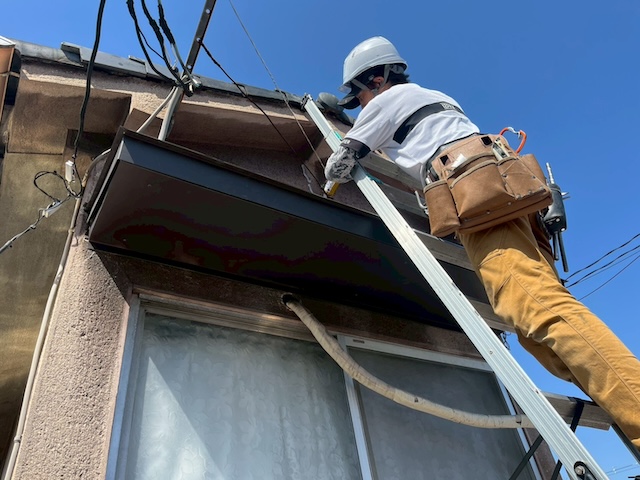 足場仮設の振動を避けてはしごを使用し高耐久な板金を設置・防水処理する職人