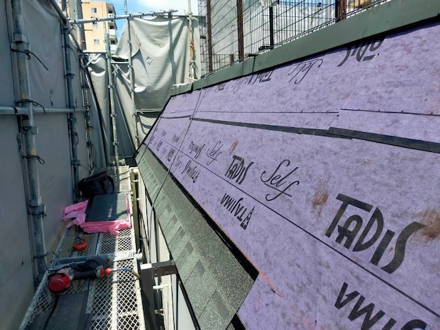 隙間なく敷き詰められた紫色の粘着系ルーフィングと、下部から丁寧に葺き始められた新屋根材