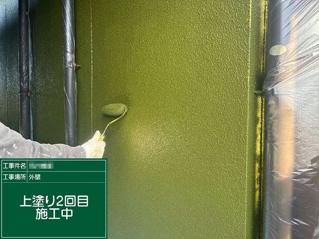 モルタル外壁に上塗り塗料をローラーで塗り重ねている様子