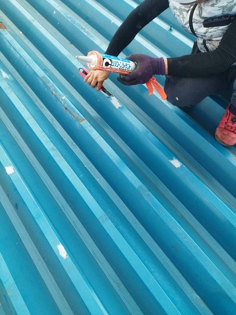 折板屋根のビス穴をコーキングで塞いでいる様子