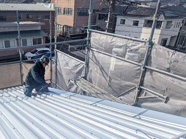 倉庫屋根カバー工事でケラバ押さえ金物を取り付けている様子