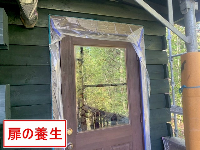 北杜市で別荘（ログハウス）の外壁塗装時に玄関扉に養生をかける様子