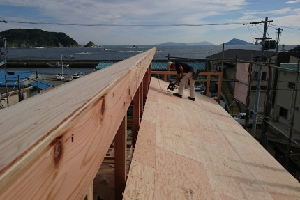 差し掛け招き屋根に板が張られて形が見えてきました。遠景に伊勢湾の水面が見えます。