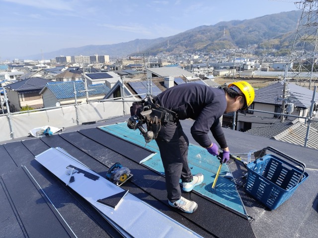 八尾市神宮寺の戸建て住宅 屋根カバー工法の棟板金設置 職人がメジャーで正確に寸法を計測している様子