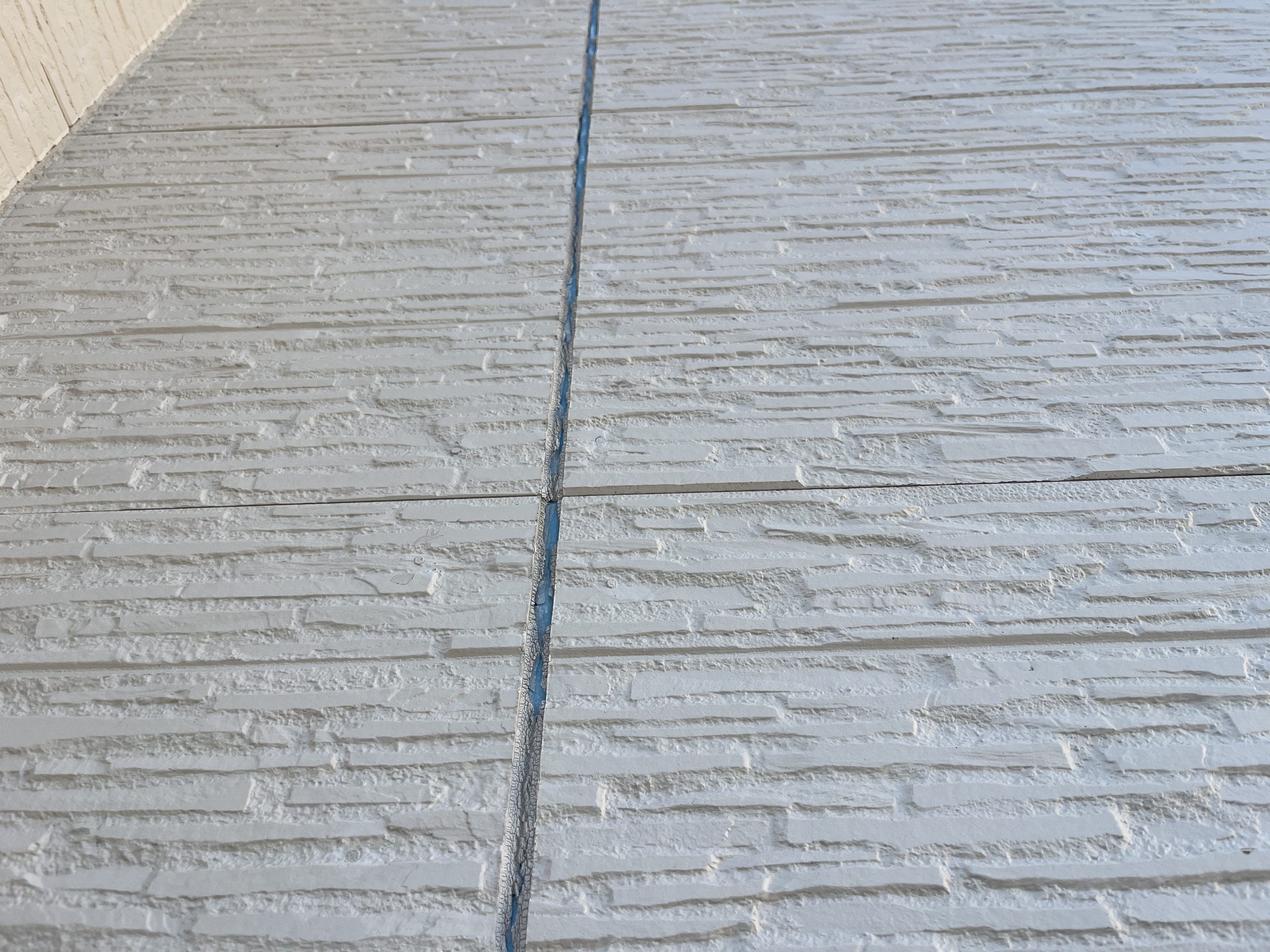 上の方までシーリングが剥がれた白い外壁