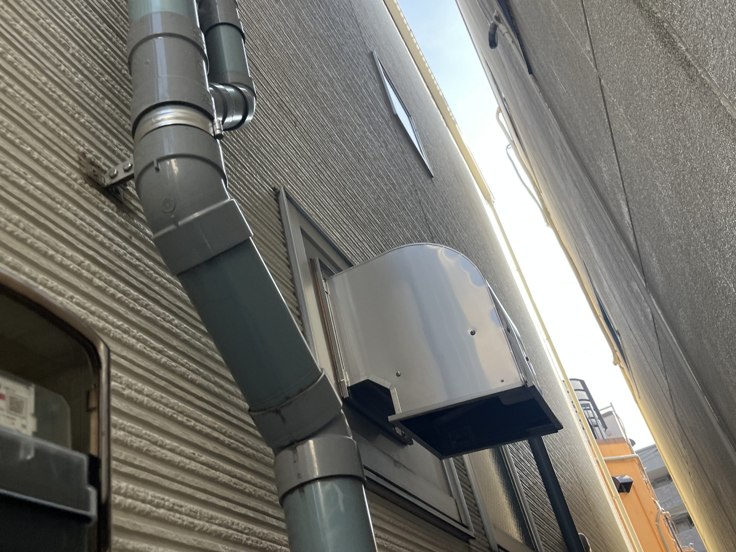 白い外壁に固定されている塩ビ管と換気扇のフード