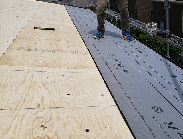 屋根に野地板とルーフィングを貼る職人