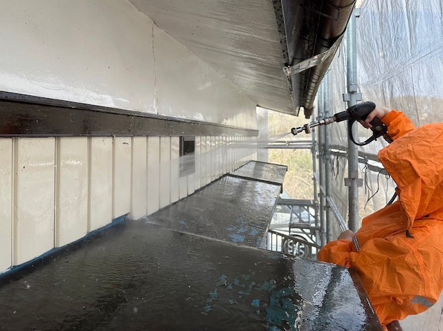 オレンジ色のカッパを着て芸壁洗浄を行うスタッフ