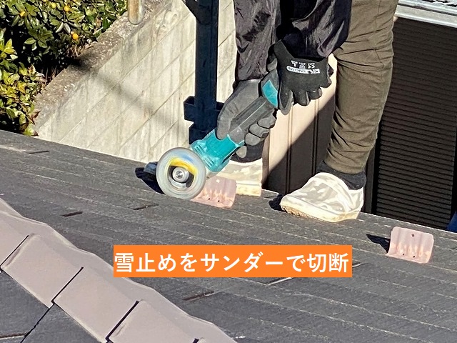 スレート屋根に設置されて雪止めをサンダーでカットする職人