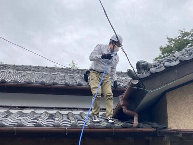 入母屋玄関に登り、雨漏り箇所を特定する為の散水調査を行うスタッフ