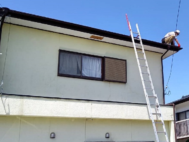 屋根に梯子を架け、軒先で作業を行う街の屋根やさん水戸店のスタッフ