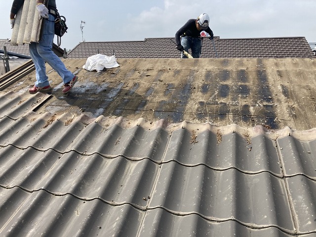 撤去した屋根材を運ぶ職人と、清掃する職人