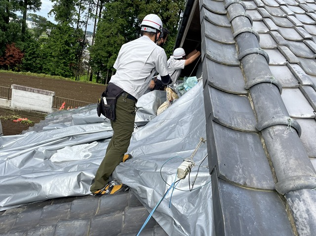 屋根にシルバーシートを掛けるスタッフ
