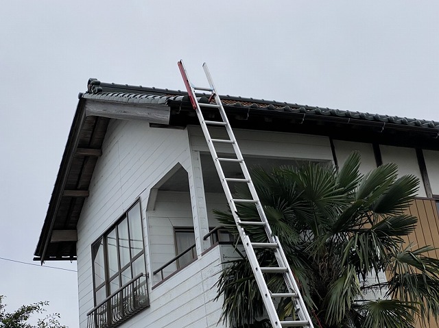 二階の瓦屋根の軒先に二連梯子を掛けた様子