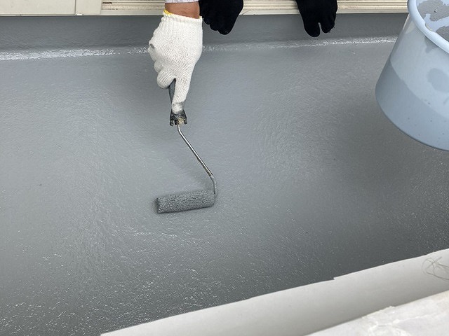 ベランダにローラーでトップコートを塗布する職人