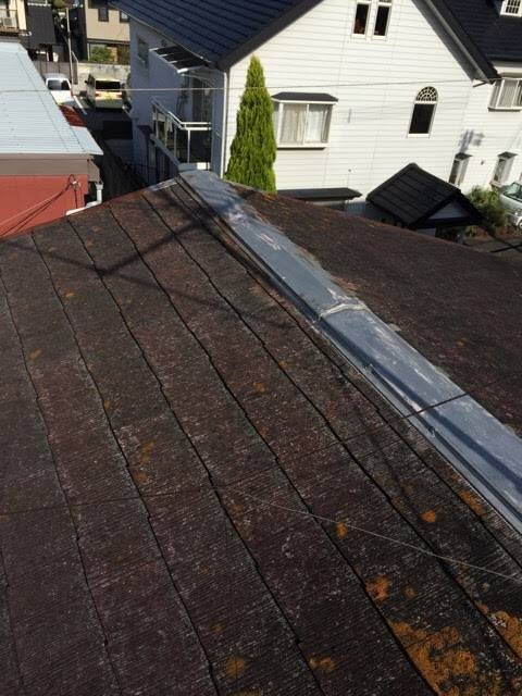 スレート屋根の棟板金の浮きと全体的な劣化状況。屋根に上がってのプロによる診断中の様子