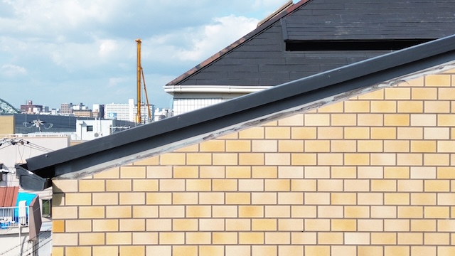 外壁と屋根の取り合い部分の側面図。雨水が集中しやすいため、シーリングのみの防水では不十分。板金の「立ち上がり」による物理的なブロック（二次防水）が推奨される。