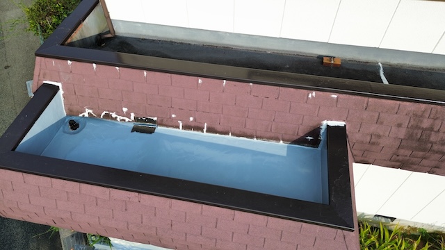 屋根の箱樋（はこどい）部分とパラペット板金の現況。既存の防水層（青色）や黒色の笠木板金の納まり、および排水ドレン周辺に詰まりや劣化がないかを確認している調査画像。