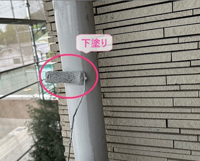 テナント建物の鼻隠しの部分塗装で竪樋に下塗り材を塗っている様子