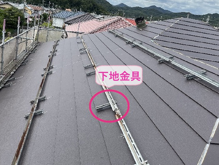 屋根重ね葺きでソーラーパネルの新しい下地金具を屋根材に挟み込んで取り付けている様子