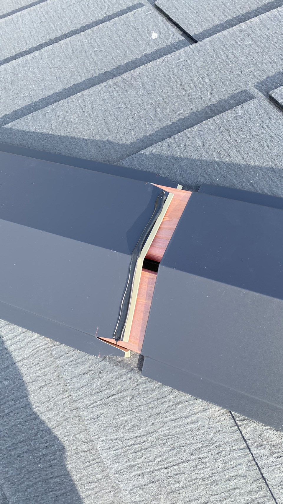 神戸市西区での板金工事で棟板金のジョイントにコーキングを挟んでいる様子