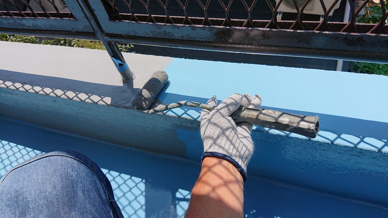 ひび割れたベランダ床に防水工事の仕上げとしてトップコートを塗っている様子