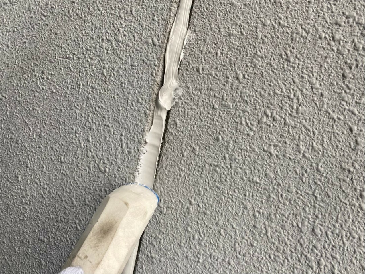 神戸市中央区でのコーキング打ち替え工事で外壁目地のコーキングを押えている様子