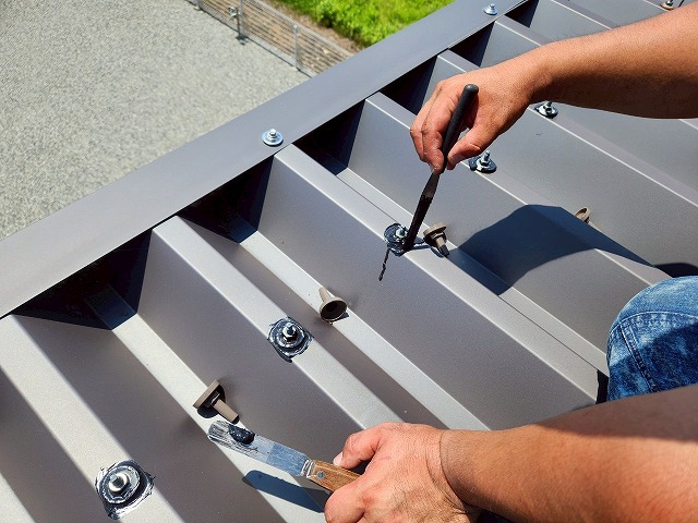 折板屋根のボルトに刷毛でプライマーを塗布している様子