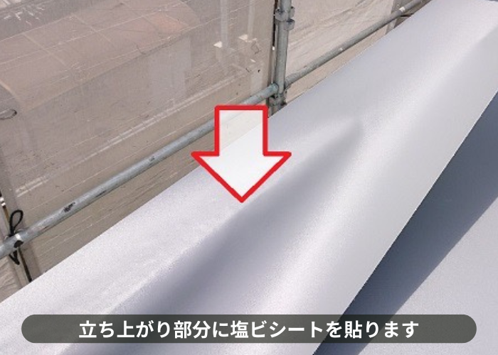 吹田市 屋上防水工事で立ち上がり部分に塩ビシートを貼っている様子